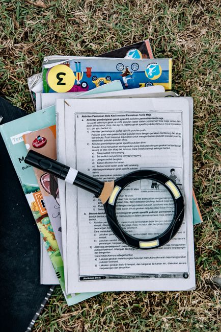 Magnifying glass on educational papers with books and grass background, outdoors.
