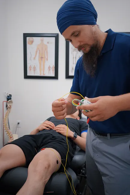 Male chiropractor applying electric stimulation therapy to a patient's leg in a modern clinic setting.