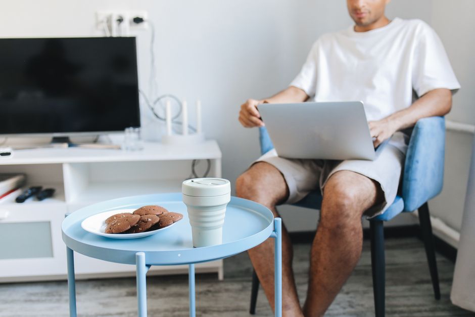 Man in a casual setting using laptop with cookies and cup nearby.