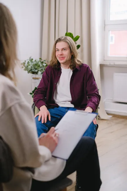 Man in a maroon jacket engages in a conversation during a therapy session indoors.