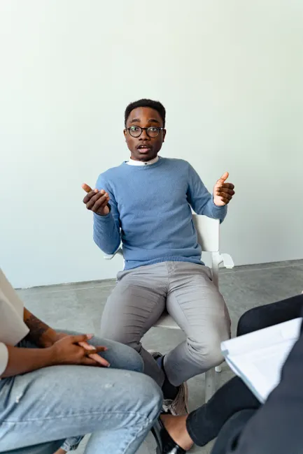 Man in blue sweater leading a group therapy discussion indoors.