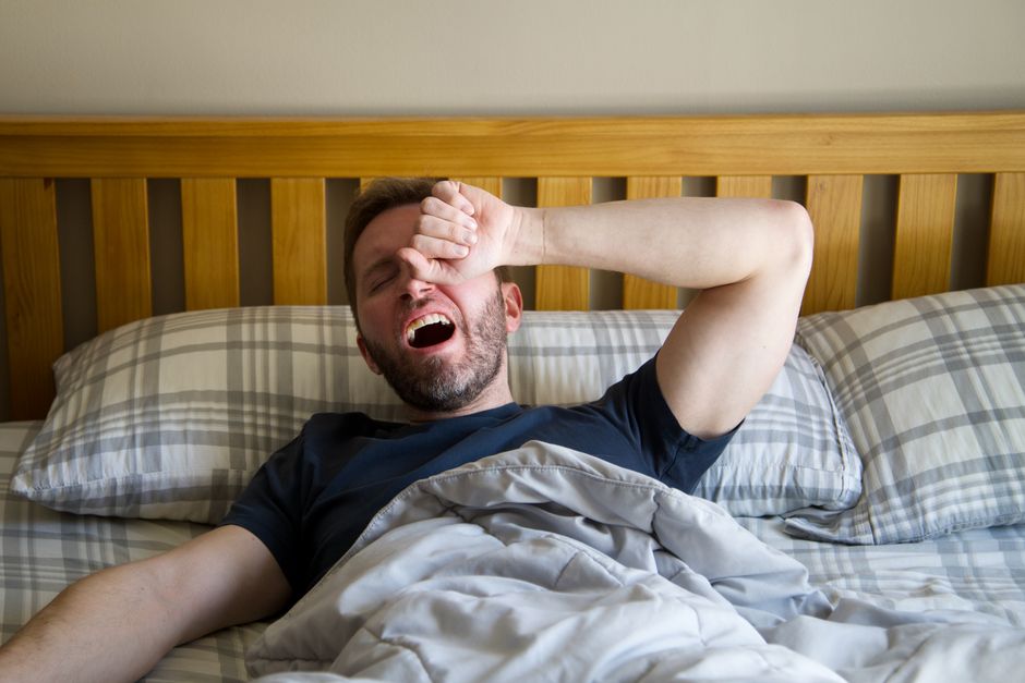Man yawning and waking up in bed, starting a new day with the morning light.