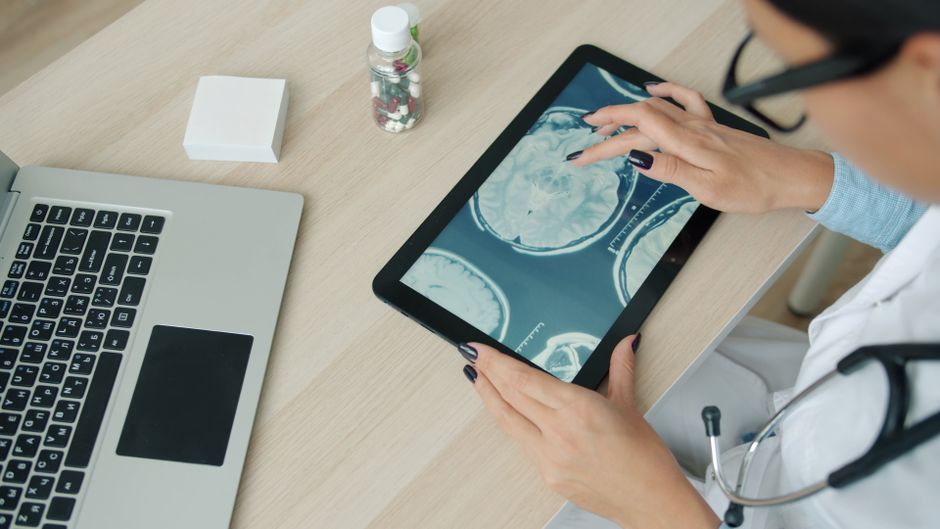 Medical professional examines MRI brain scans on a tablet, indicating modern healthcare technology.