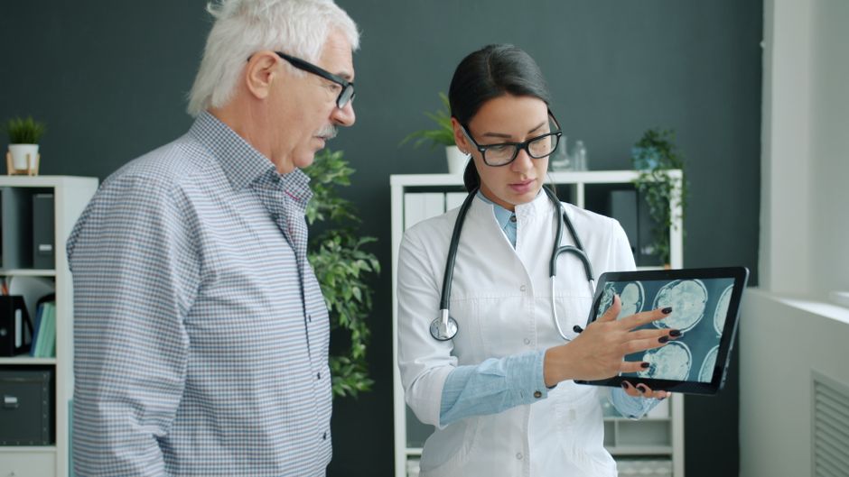 Medical professional reviewing brain scans with an elderly man in a clinic.