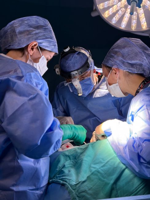 Medical team in a hospital operating room performing surgery under bright surgical lights.