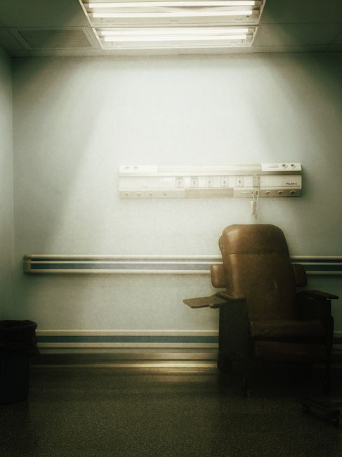 Moody hospital room featuring an empty chair under bright fluorescent lights.