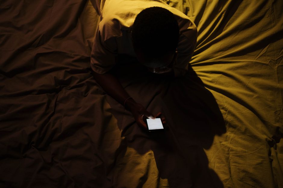 Procrastination du coucher : quand la nuit devient un espace de liberté Overhead shot of a person using a smartphone on a bed, creating a moody atmosphere.
