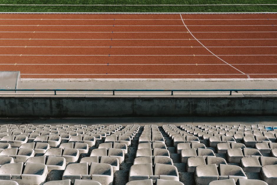 Rows of empty stadium seats with a view of the running track under daylight.