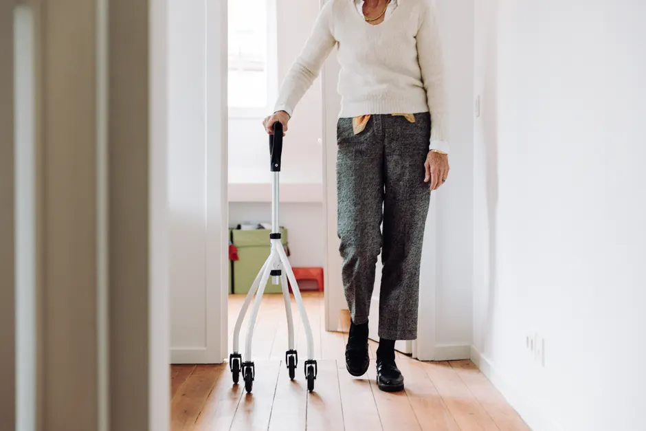 Forme mentale : entraîner le cerveau sans oublier la vie réelle Senior adult walking indoors with a rollator, promoting mobility and independence.