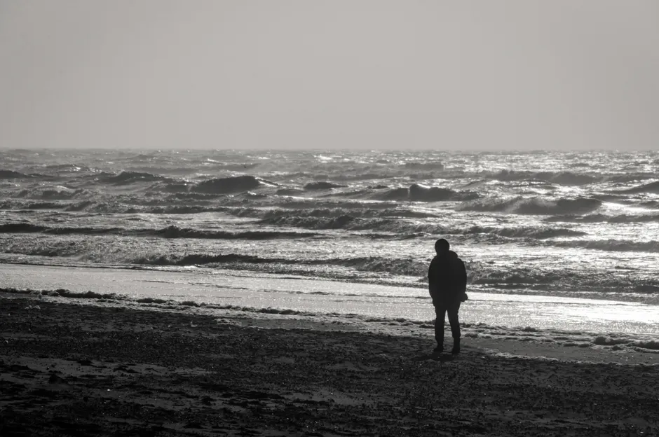 Silhouette of a person walking along a serene beach at sunset, reflecting solitude.