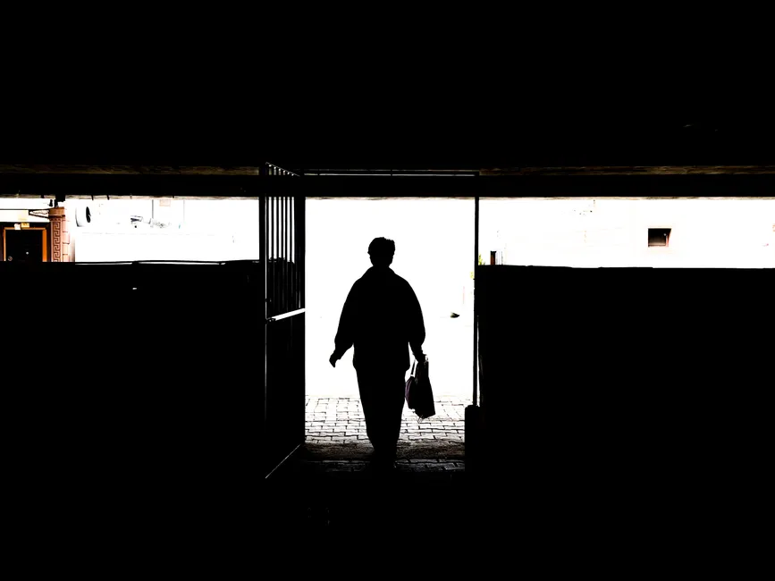 Silhouette of a person walking out of a dark passage into the light outdoors.