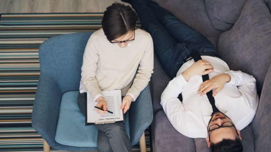 Therapist holding session with patient reclining on sofa, discussing mental wellness.
