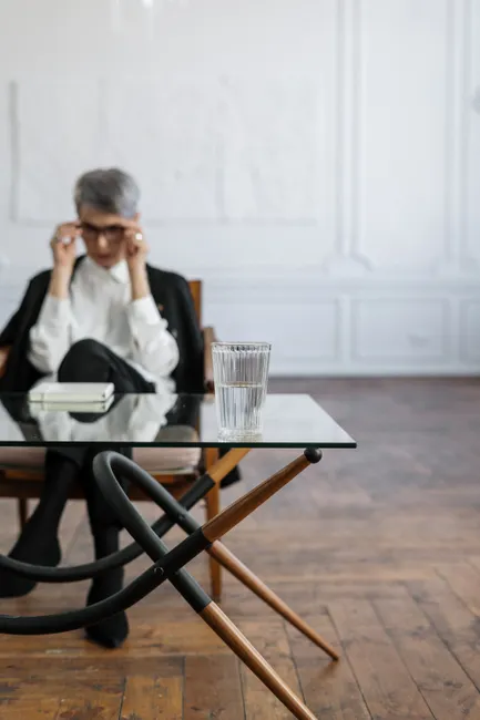 Therapist in a modern office sitting by a glass table with a water glass.