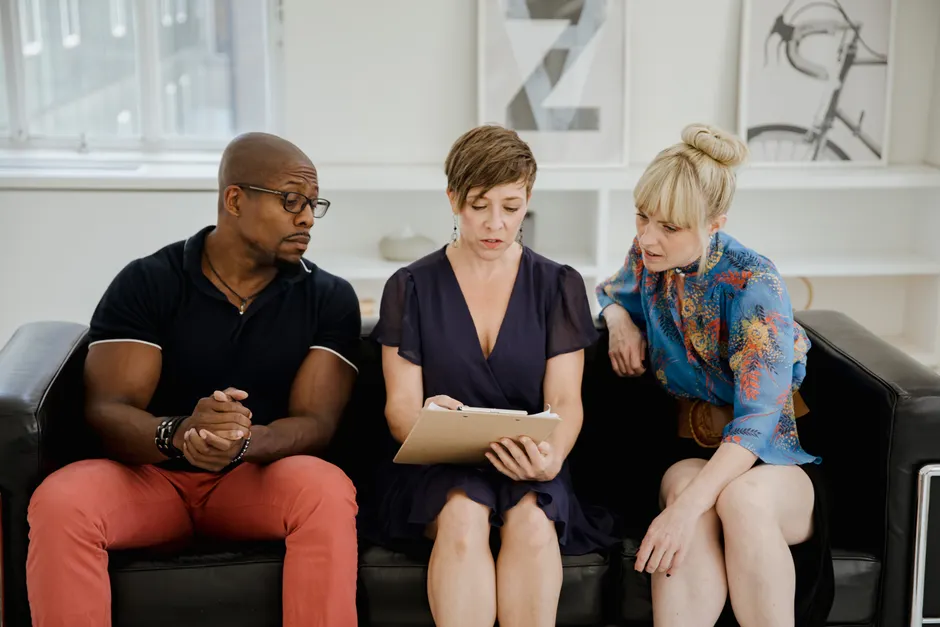 Three adults discussing content on a clipboard in a contemporary office environment.