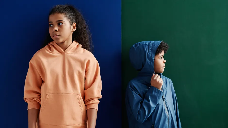 Two children wearing contrasting hoodies stand thoughtfully against a vibrant background.