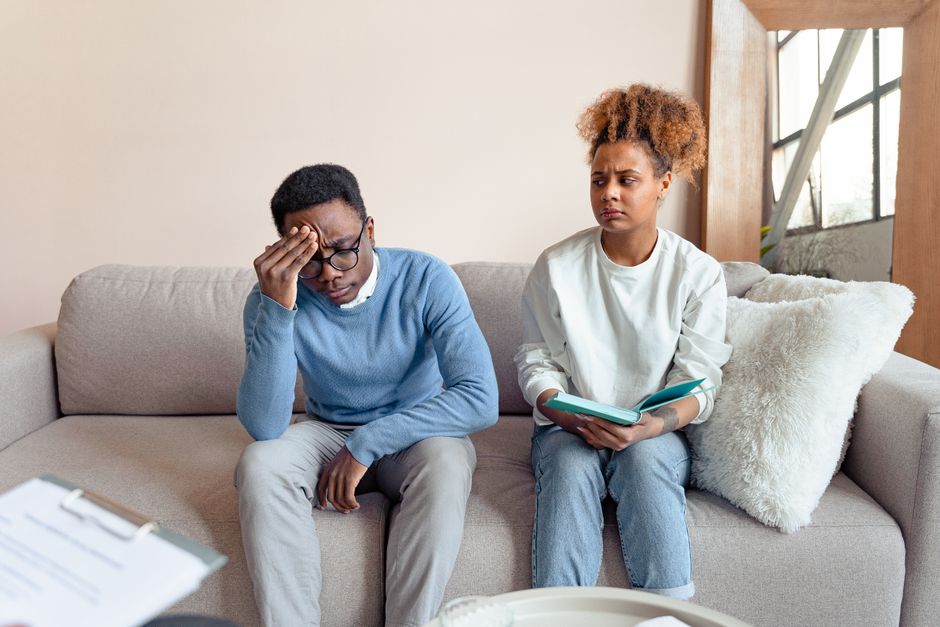 Two people sitting on a sofa indoors, engaged in a serious discussion during a therapy session.