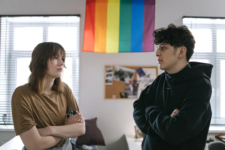 Two people talking in an office with a pride flag in the background.