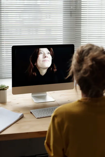Woman using desktop computer for video call from home office.