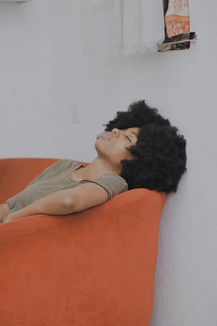 Woman with curly hair resting on an orange sofa, providing a peaceful and calming ambiance.