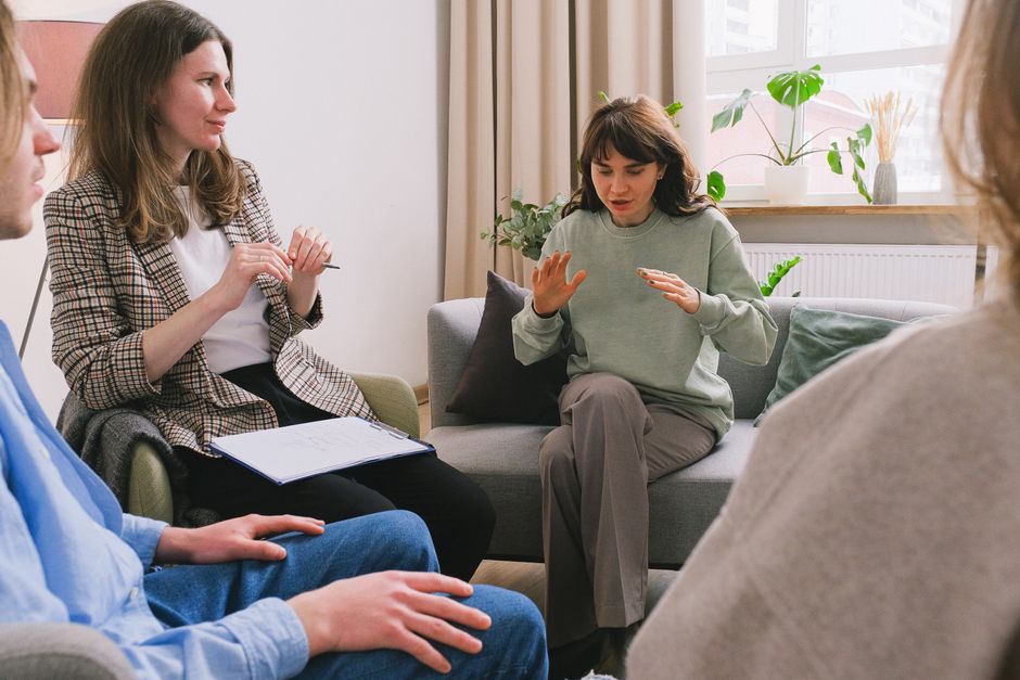 Women in casual clothes sitting on sofa and speaking during group psychotherapy session in cozy office