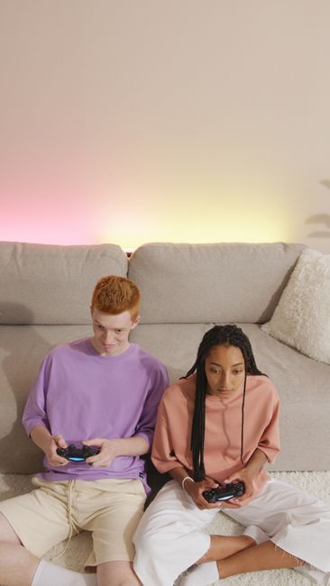Young couple sitting on floor in front of sofa playing video games indoors.