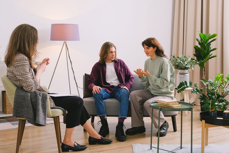 Young couple sitting on sofa and talking with woman psychologist in light room in daytime