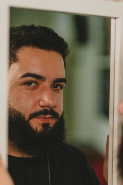A bearded man looks at his reflection in the mirror, showcasing a thoughtful expression.