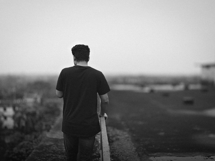 A black and white photo of a man in casual attire walking alone in a foggy environment.