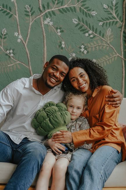 A cheerful family of three with a child hugging on a sofa indoors.