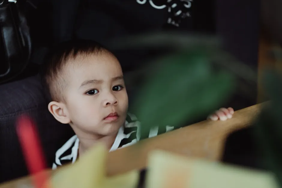 Assimilation en psychologie : quand le nouveau doit entrer dans une vieille case A child with a curious expression peeking behind a table indoors, captured in natural light.
