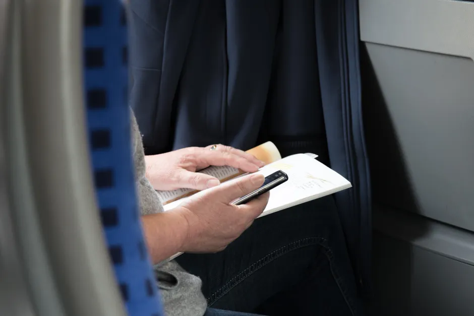 A close-up of someone reading a book indoors while holding a mobile device.