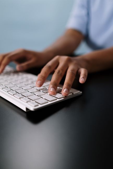 A close-up view of hands typing on a sleek white wireless keyboard on a desk.