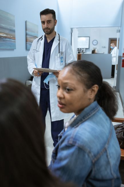 A doctor in a white coat consults a worried patient in a hospital hallway.