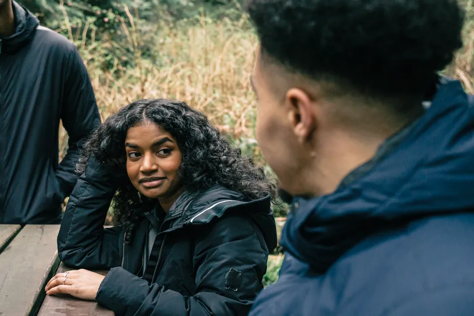 A group of friends having a relaxed conversation at a picnic table in a natural setting.