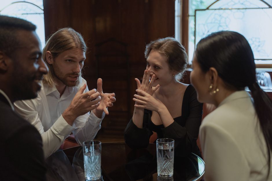 A group of friends talking and laughing around a table in a cozy indoor setting.