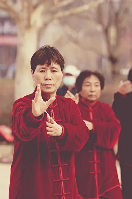 A group of people performing Tai Chi exercises outdoors, wearing red traditional outfits.