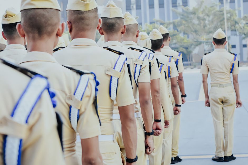 A group of soldiers in formal uniforms standing in a line at an outdoor military ceremony.