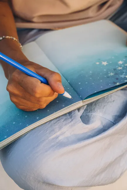 A hand holding a blue pen writing in a star-covered journal. Ideal for planning and creativity themes.
