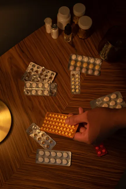 A hand reaching for blister pack amid assorted medications on a wooden table.