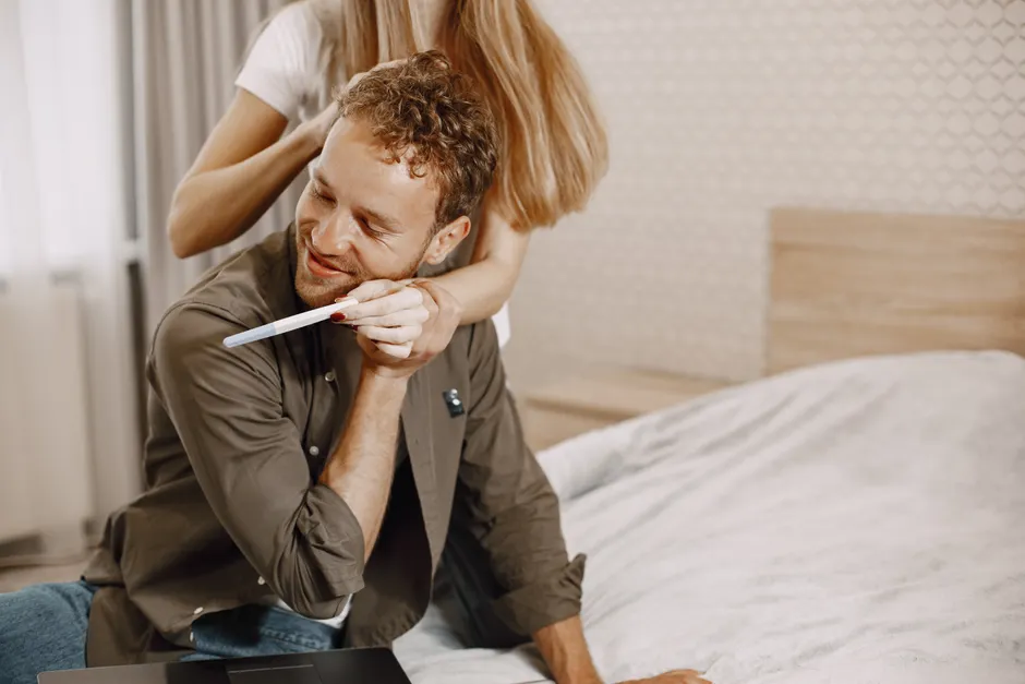 A happy couple celebrating after seeing a positive pregnancy test result in their bedroom.