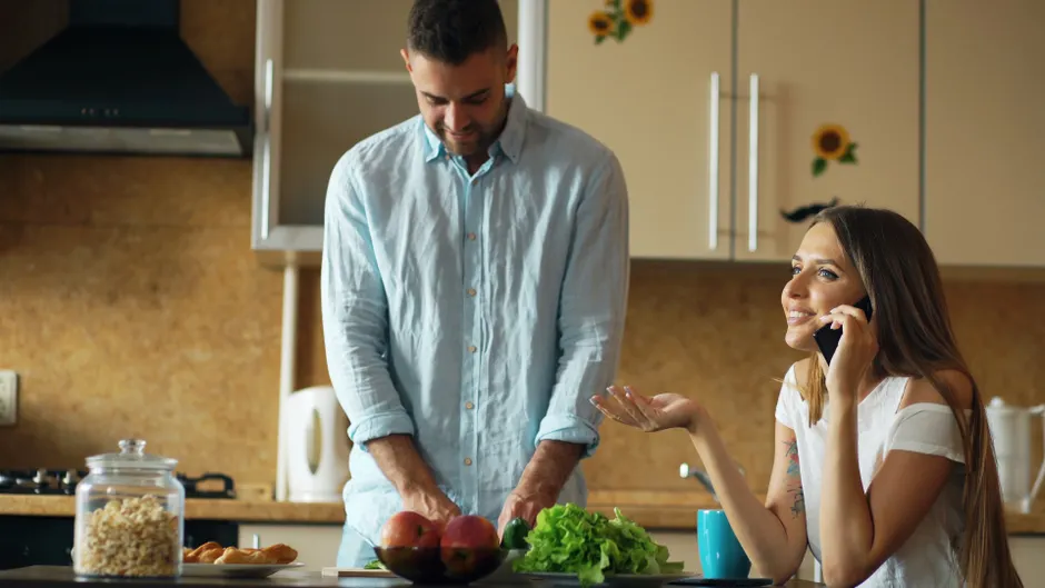 A happy couple preparing a meal together in a modern kitchen while talking on the phone.