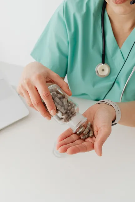 A healthcare worker in teal scrubs holding supplement capsules in their hand.