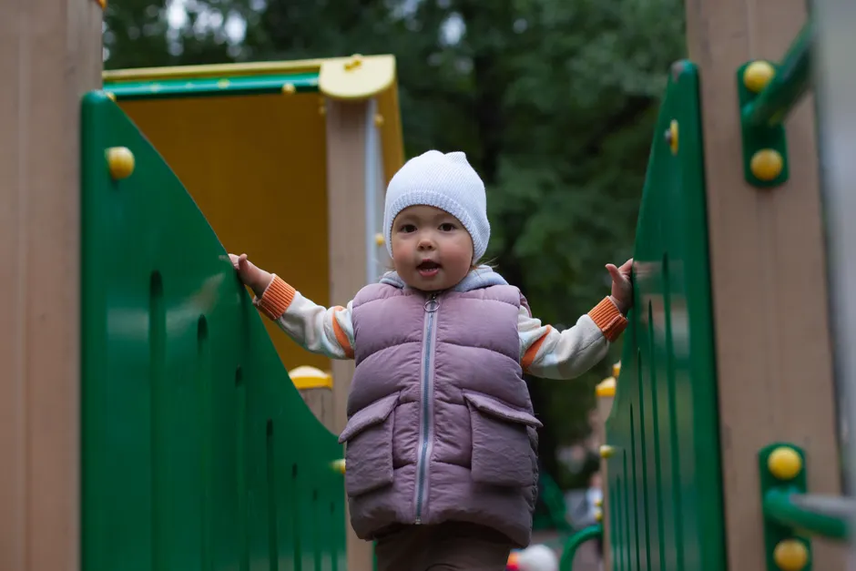 A joyful toddler playing outdoors at a colorful playground in warm attire.