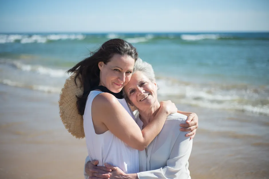A loving mother and daughter share a warm embrace on a sunny beach in Portugal, signifying family bonding.
