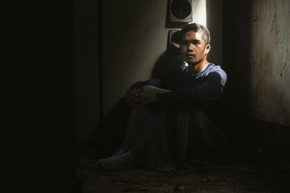 A man sits alone in a dark room, softly illuminated to convey solitude.