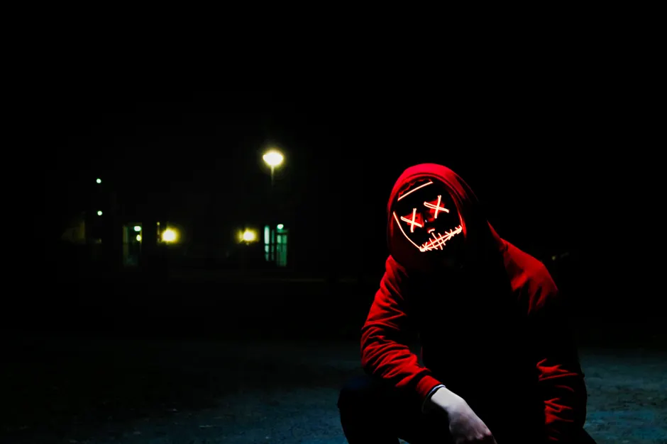 Samhainophobie : quand la peur d’Halloween devient envahissante A mysterious person wearing a red hoodie and creepy LED mask at night in a dark outdoor setting.