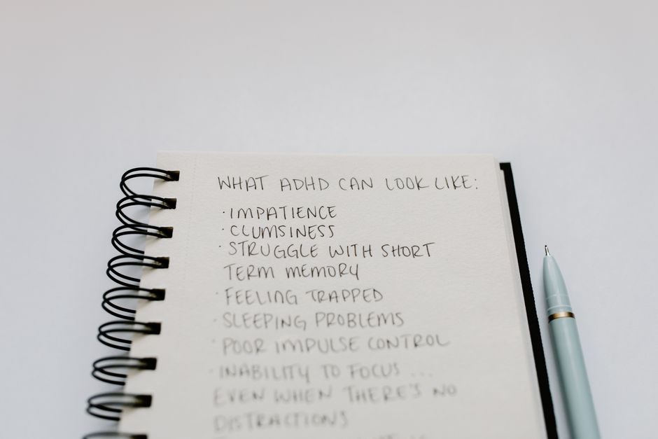A notebook with handwritten ADHD symptoms like impatience and focus issues.