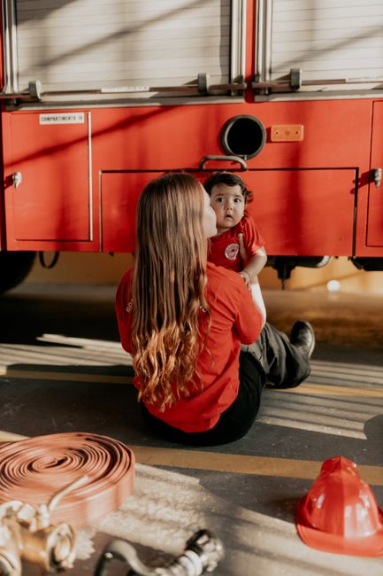 A parent and child sitting near fire equipment with a firetruck in sunlight.