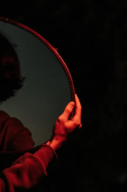 A partial view of a person holding a mirror reflecting dim light, creating a mysterious ambiance.