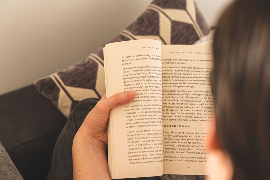 A person enjoys a relaxing reading session indoors, holding an open book on a comfy couch.